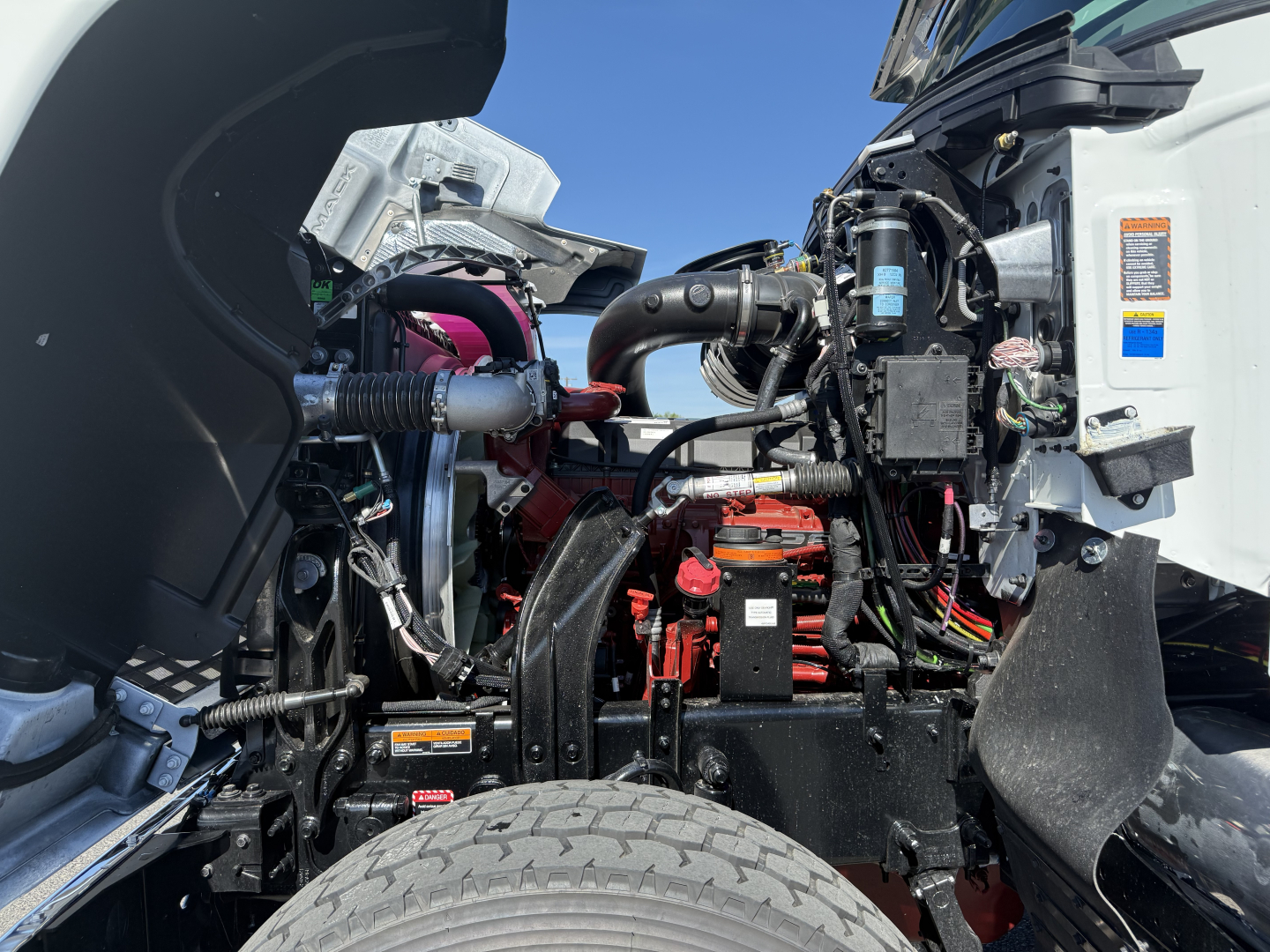 Truck engine bay with visible components: air intake, wiring, red battery/relay area, hoses, and label stickers.