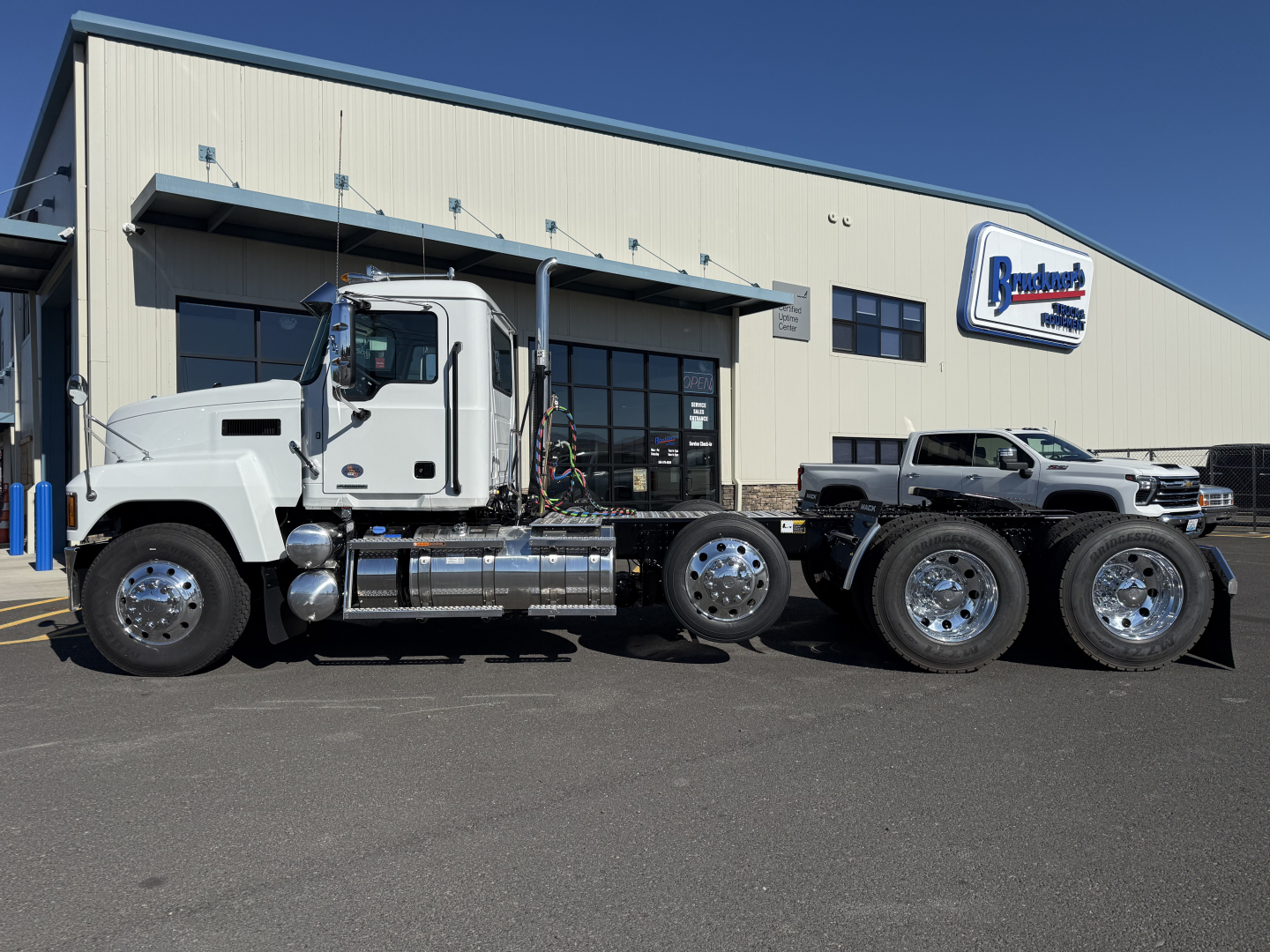 2027 Mack PI84T conventional daycab truck side view showing cab, chassis, and dual rear axles in front of dealership building.