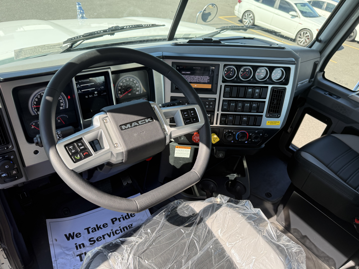 Mack PI84T dash and steering wheel interior showing instrument cluster, control panel, and steering wheel with Mack logo; plastic seat cover and dashboard buttons visible.