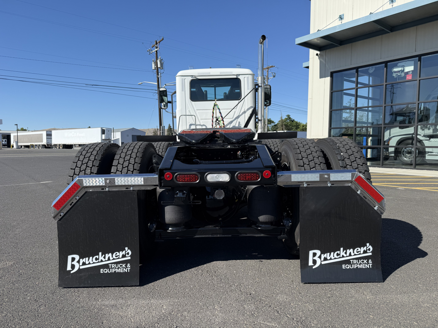 Rear view of a new Mack PI84T conventional daycab truck showing dual rear wheels and mudflaps with Bruckner's Truck & Equipment branding.