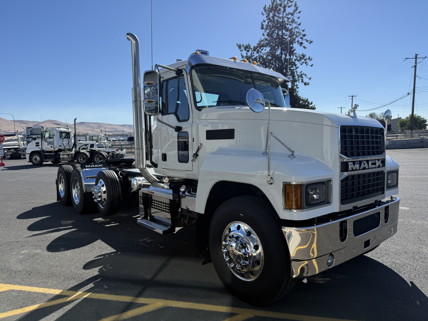 Mack PI84T conventional daycab truck side view showing white cab, chrome exhaust stacks, large mirrors, and dual rear axles; Mack badge on grille.