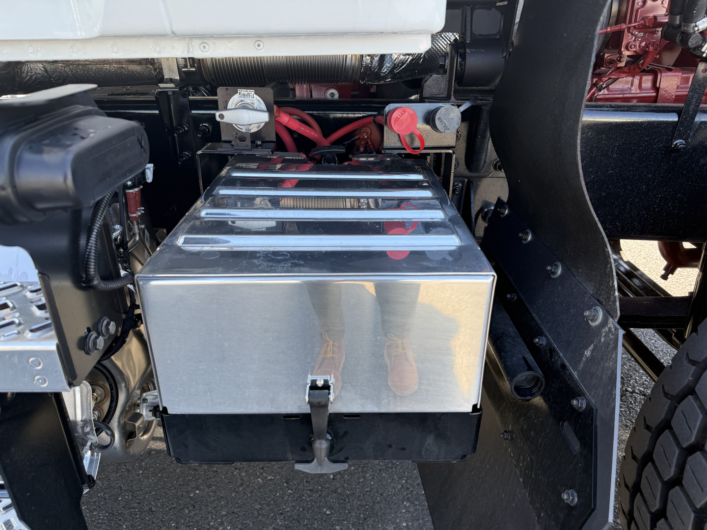 Mack PI84T truck engine bay showing a polished metal toolbox with chrome top and black bottom, surrounding chassis and power lines.
