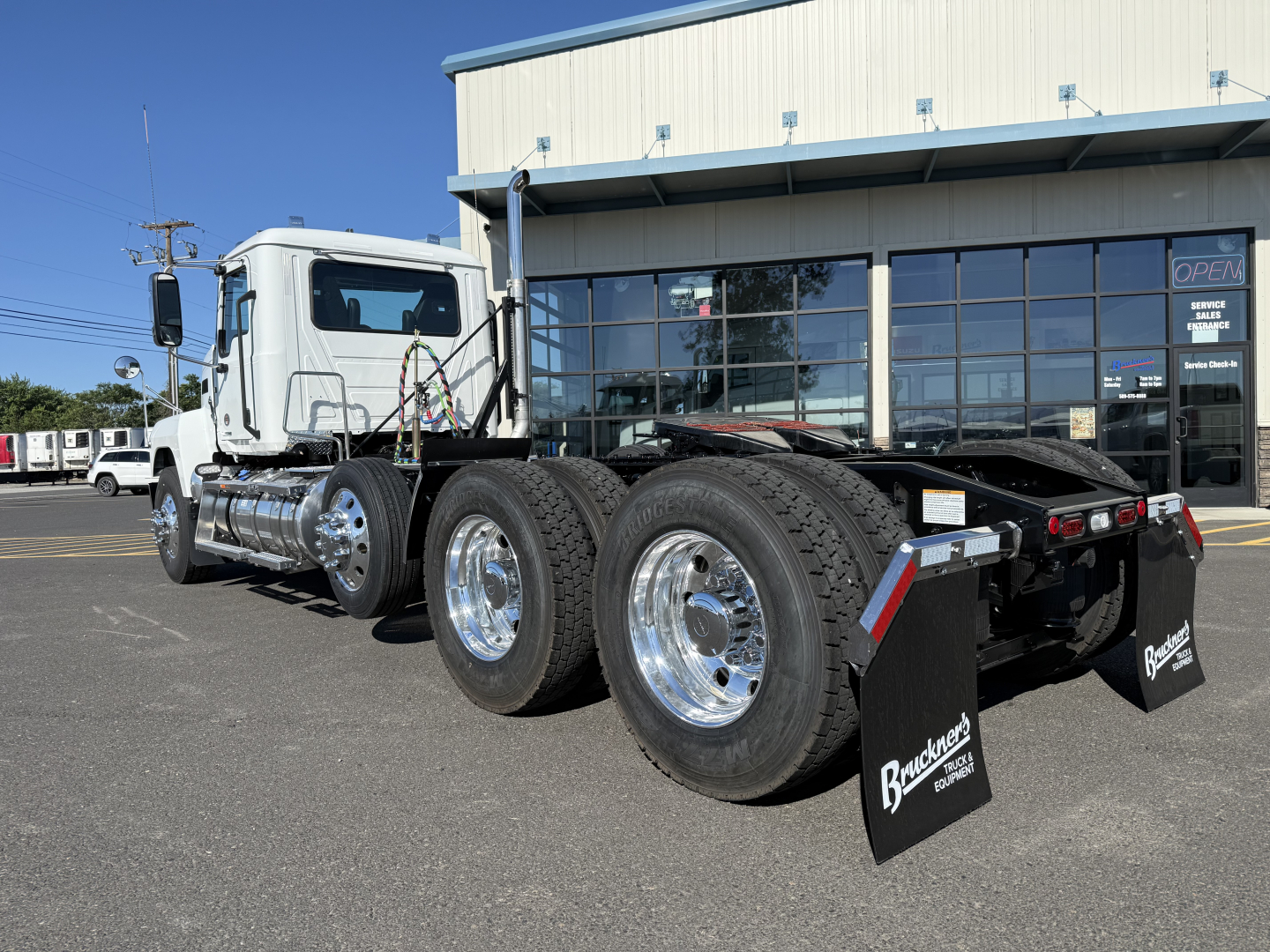 Mack PI84T conventional daycab truck chassis and dual rear axles with chrome wheels parked outside a dealership.