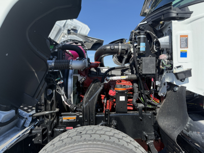 Truck engine bay with visible components: air intake, wiring, red battery/relay area, hoses, and label stickers.