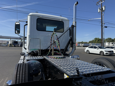 New Mack PI84T conventional daycab truck, side view of the cab and diamond plate deck, vertical exhaust, wiring harness over hood, front tires visible.