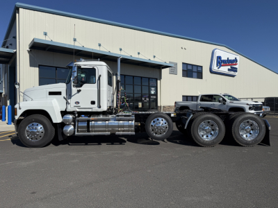 2027 Mack PI84T conventional daycab truck side view showing cab, chassis, and dual rear axles in front of dealership building.
