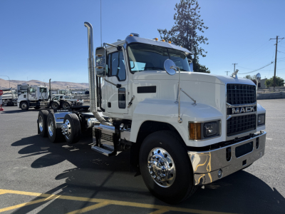 Mack PI84T conventional daycab truck side view showing white cab, chrome exhaust stacks, large mirrors, and dual rear axles; Mack badge on grille.