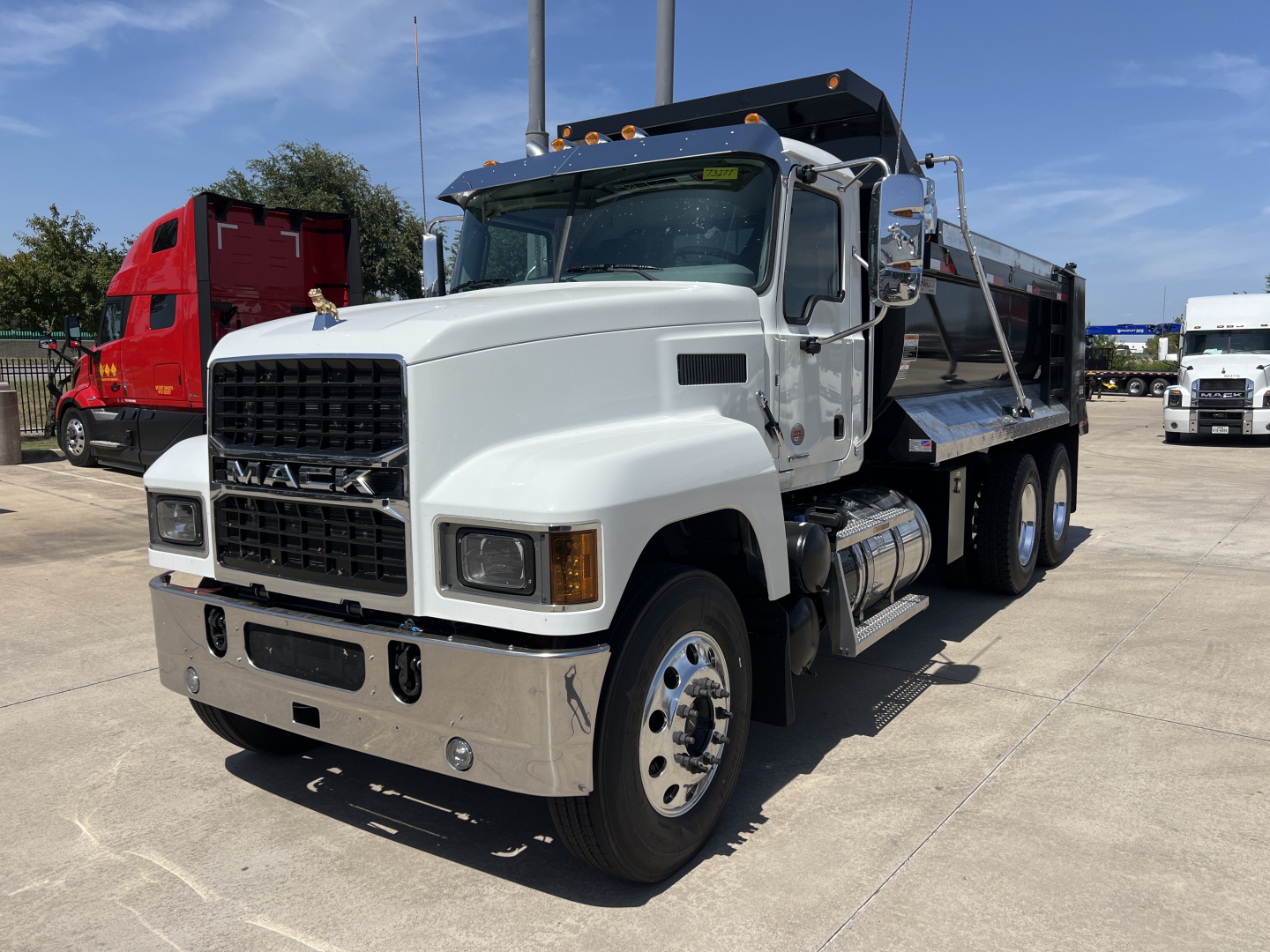 Mack PI64 front-left view showing dump truck with white cab and black grille, chrome bumper, dual rear axles, and dump bed.
