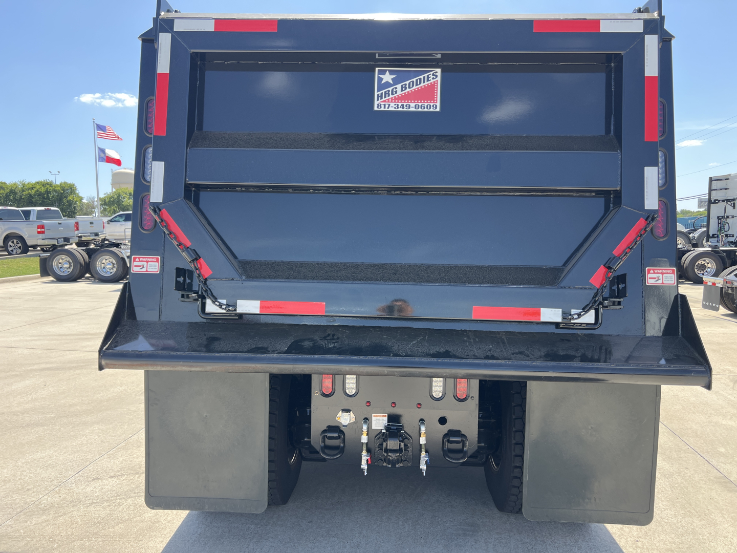 Mack PI64 dump truck rear showing hydraulic tailgate, rear bumper, and two hitch points with warning decals.
