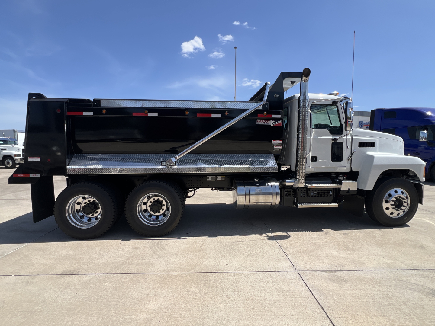 Mack PI64 dump truck side view showing black dump body, chrome tandem rear wheels, and chrome fuel tank.
