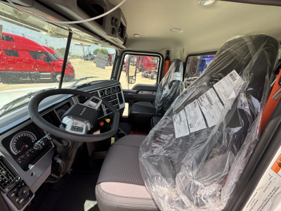 Interior of a 2027 Mack PI64 dump truck cab showing steering wheel, dashboard, and seating with plastic covers on seats.