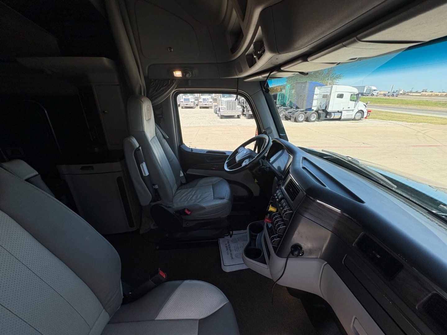 Truck cab interior of a 2025 Peterbilt 579 showing driver seat, steering wheel, dashboard, and center console from the passenger side door open.