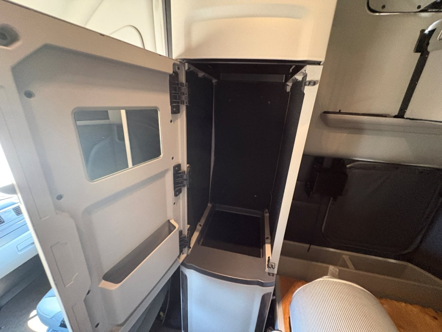 Peterbilt 579 cab interior storage compartment with open compartment door and empty under-dash space; visible are the cabinet door, hinge, and interior cavity.