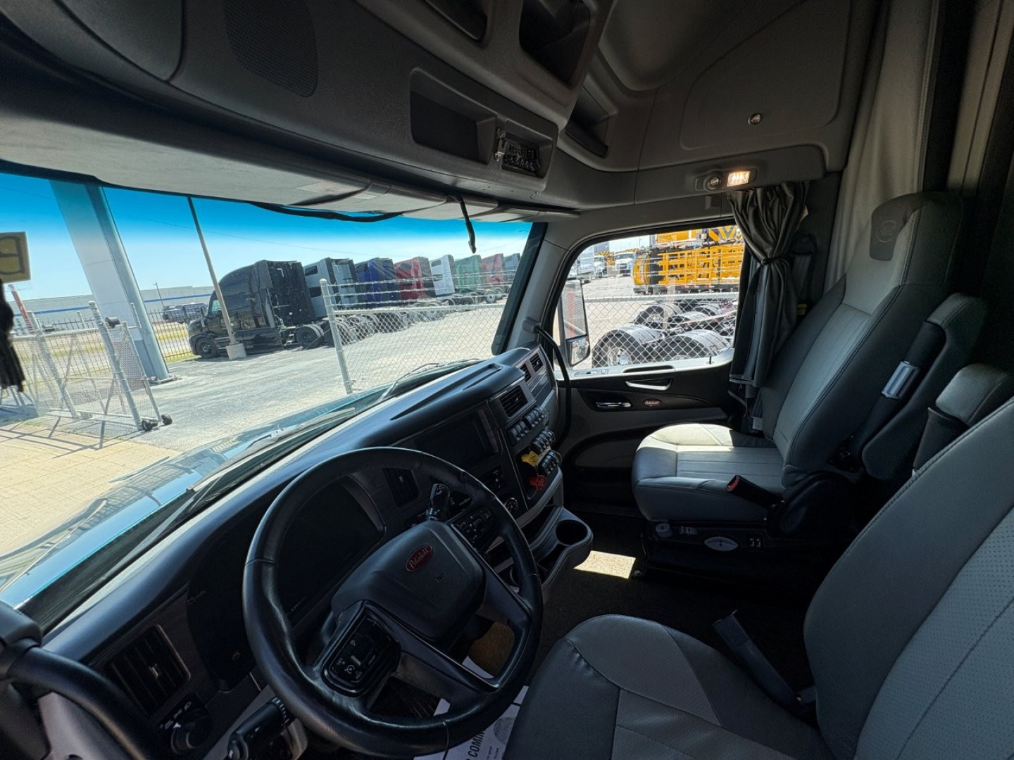 Peterbilt 579 truck interior cab dash and steering wheel showing driver seat and passenger seat, truck cab with overhead storage and window view