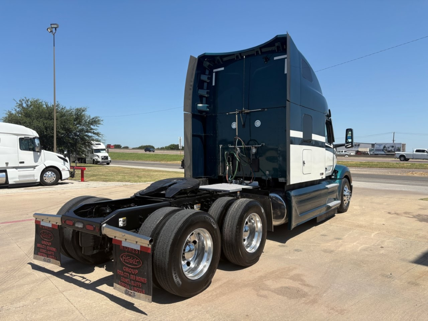 Peterbilt 579 truck tractor rear/side view showing sleeper cab and triple rear axles with wheels and fifth wheel coupling.