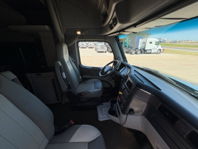 Truck cab interior of a 2025 Peterbilt 579 showing driver seat, steering wheel, dashboard, and center console from the passenger side door open.