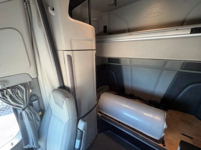 Peterbilt 579 cab interior view showing sleeper area and door sill with light fabric upholstery and cargo in the cabin.