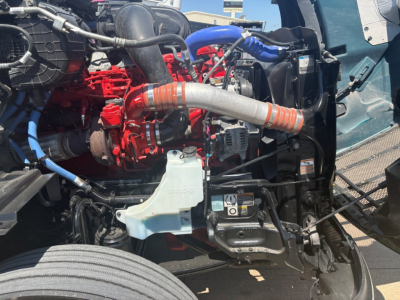 Peterbilt 579 engine bay showing red engine components, blue hoses, and a large curved orange hose connected to the radiator area.