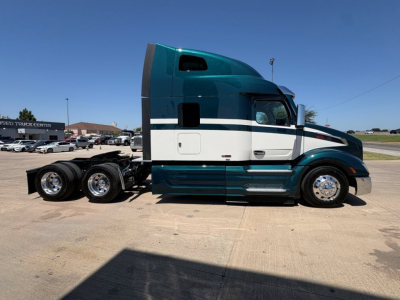 Peterbilt 579 tractor in teal and white, side view showing sleeper cab, 6-wheeled rear trailer chassis, clear blue sky.