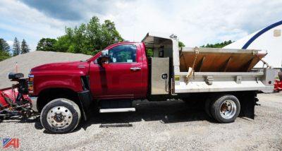Dump truck with plow and salt spreader in red cab and white bed, side view.