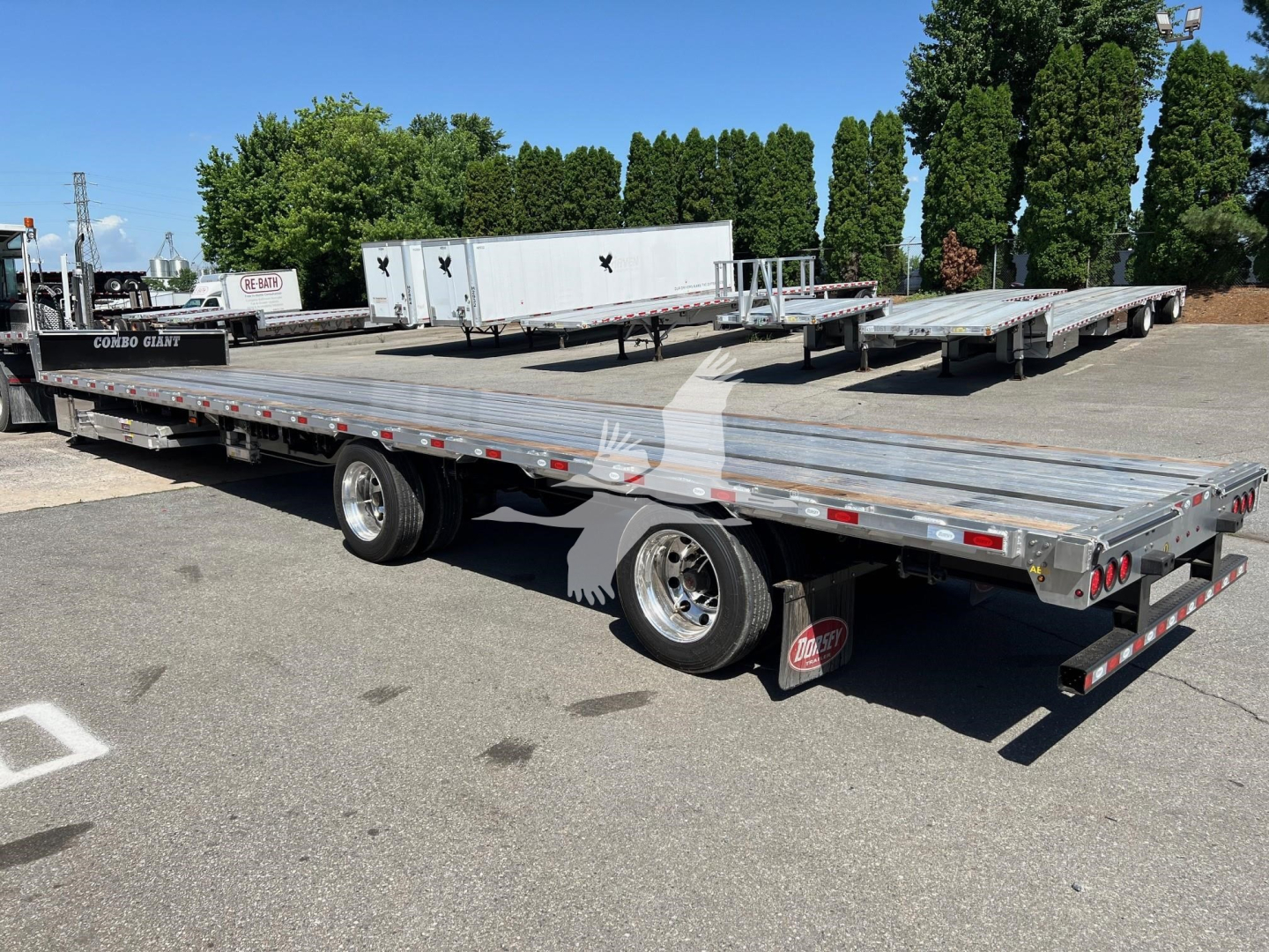 Flatbed trailer with ramp kit and multiple deck sections in an outdoor lot, with trees in background.