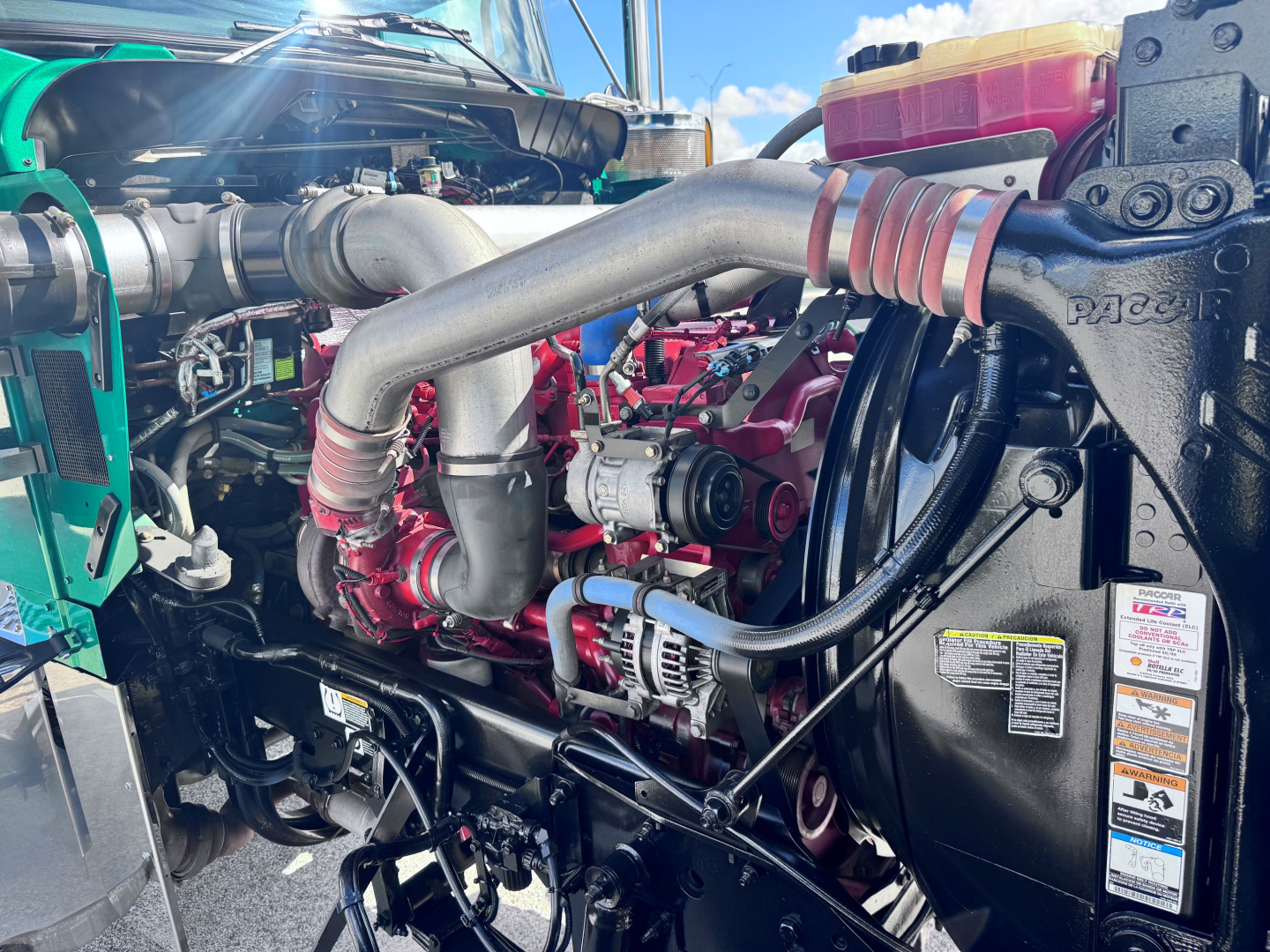 Kenworth W900L engine bay showing turbocharger, hoses, radiator hoses, and auxiliary components in a diesel engine compartment.