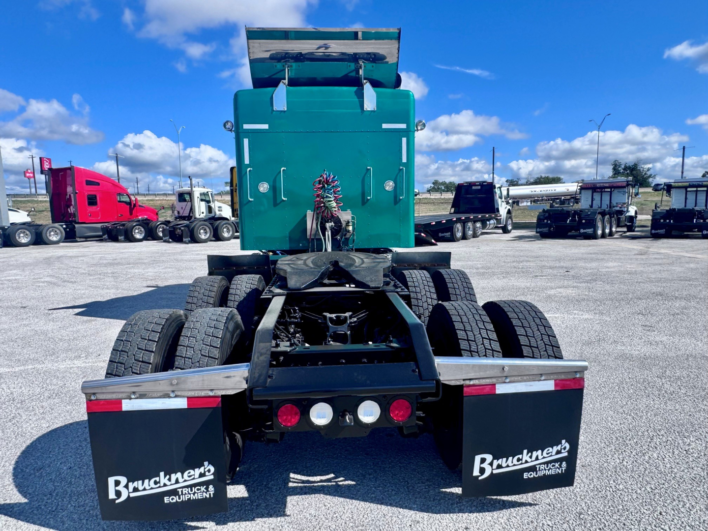 Rear view of a green Kenworth W900L tractor showing dual rear axles and mud flaps with Bruckner’s Equipment logos.