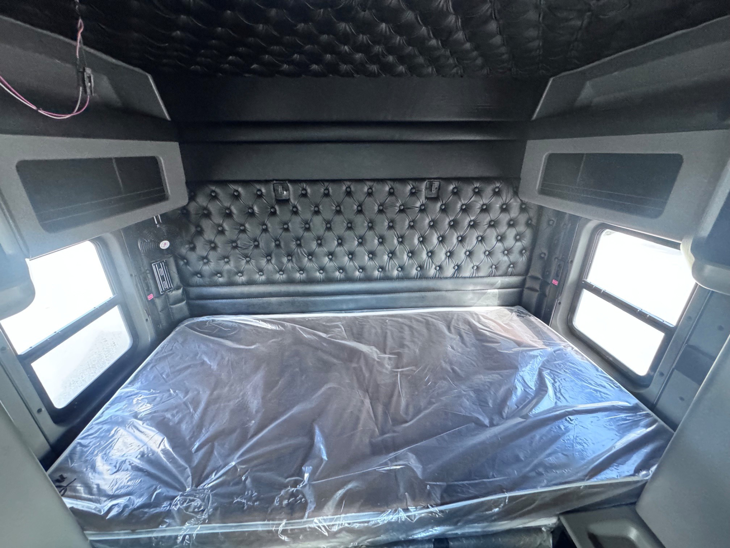 Kenworth W900L sleeper cab interior with quilted padded wall, side windows, and bed covered in plastic sheet.