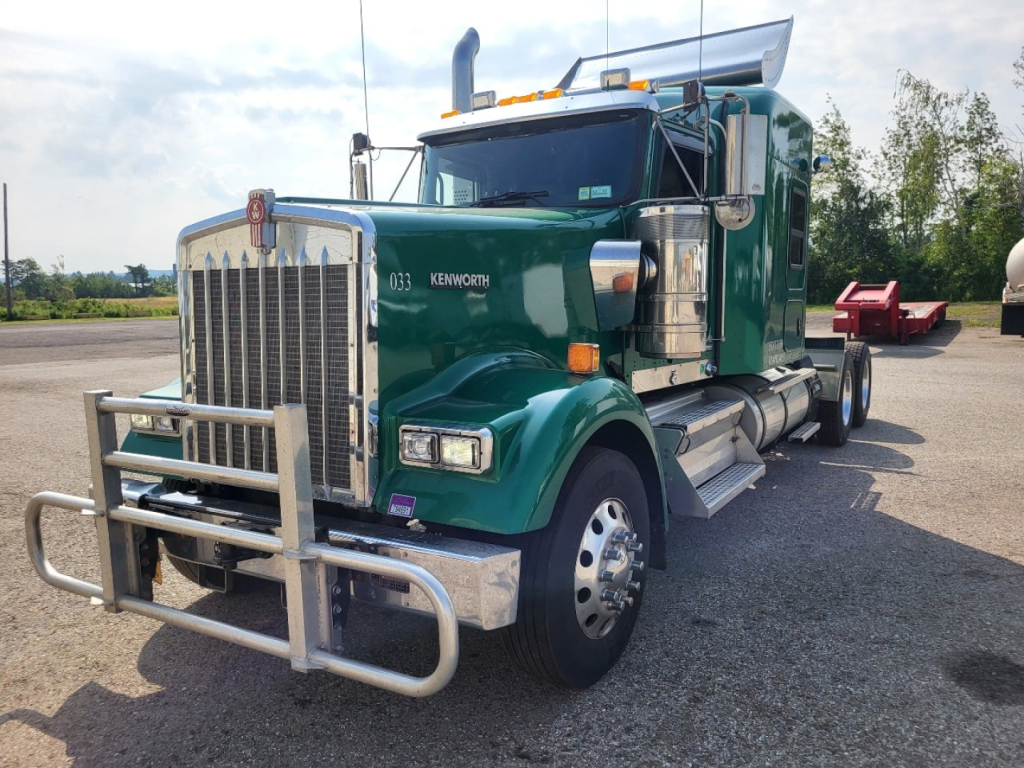 Kenworth W900L truck in green with chrome bumper and chrome exhaust, front grille and headlights visible.