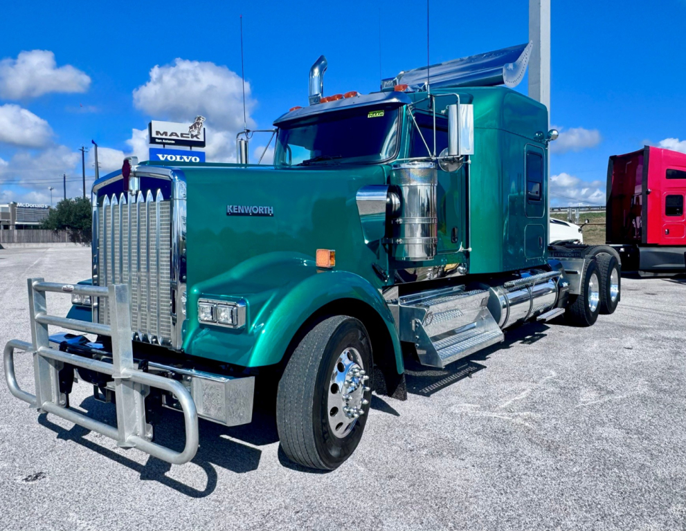 Kenworth W900L truck in green with chrome grille and sleeper cab, side view showing dual rear axles and chrome exhaust stacks.