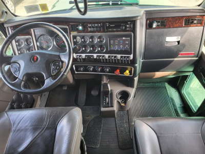 Kenworth W900L cabin dashboard and steering wheel with multiple gauges, switches, and a central touchscreen; gear selector and cup holder visible.