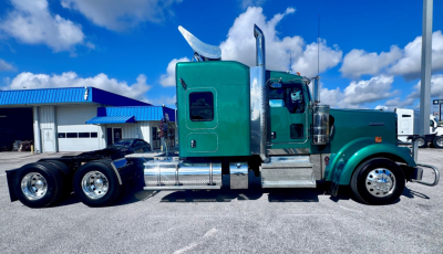 Kenworth W900L truck side view showing green cab, chrome fuel tanks, dual rear axles, and aerodynamic exhaust stacks.