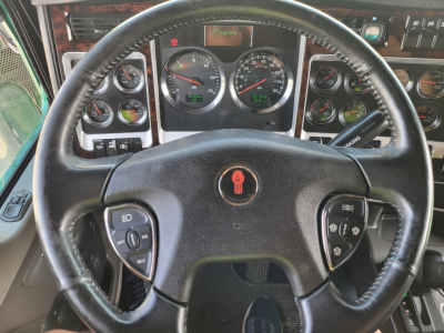 Kenworth W900L steering wheel view of dashboard showing multiple gauges and control stalks.
