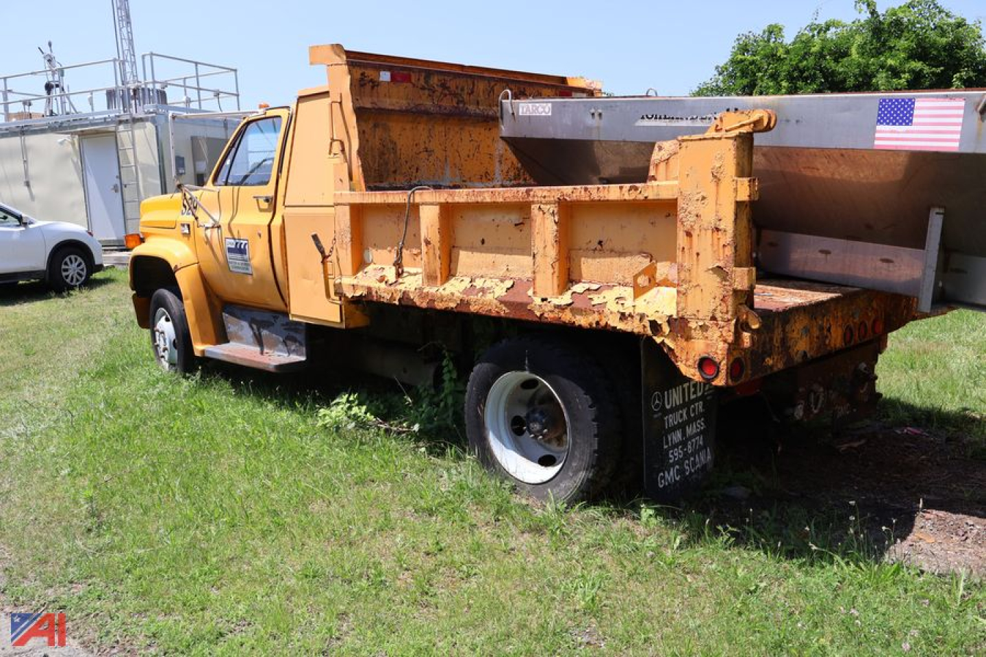 GMC TopKick C6500 dump truck in-service showing orange dump bed and right-side taillight area with weathered metal and American flag decal