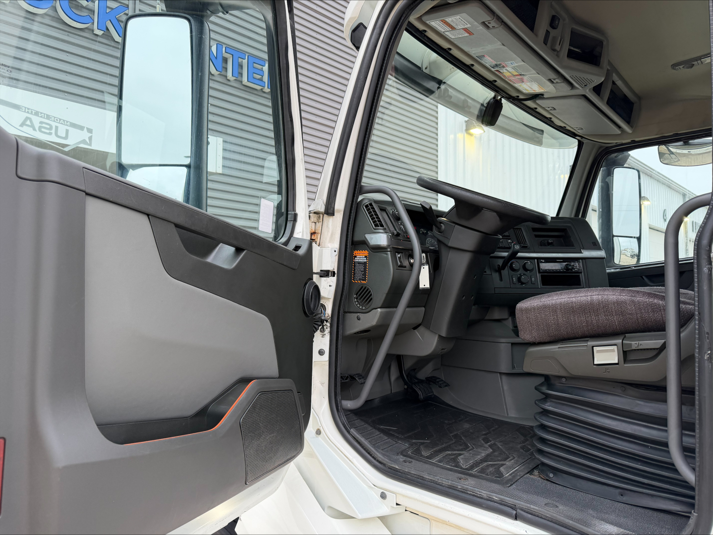 Truck cab interior showing steering wheel and dashboard of a Volvo VNL300 daycab with open door.