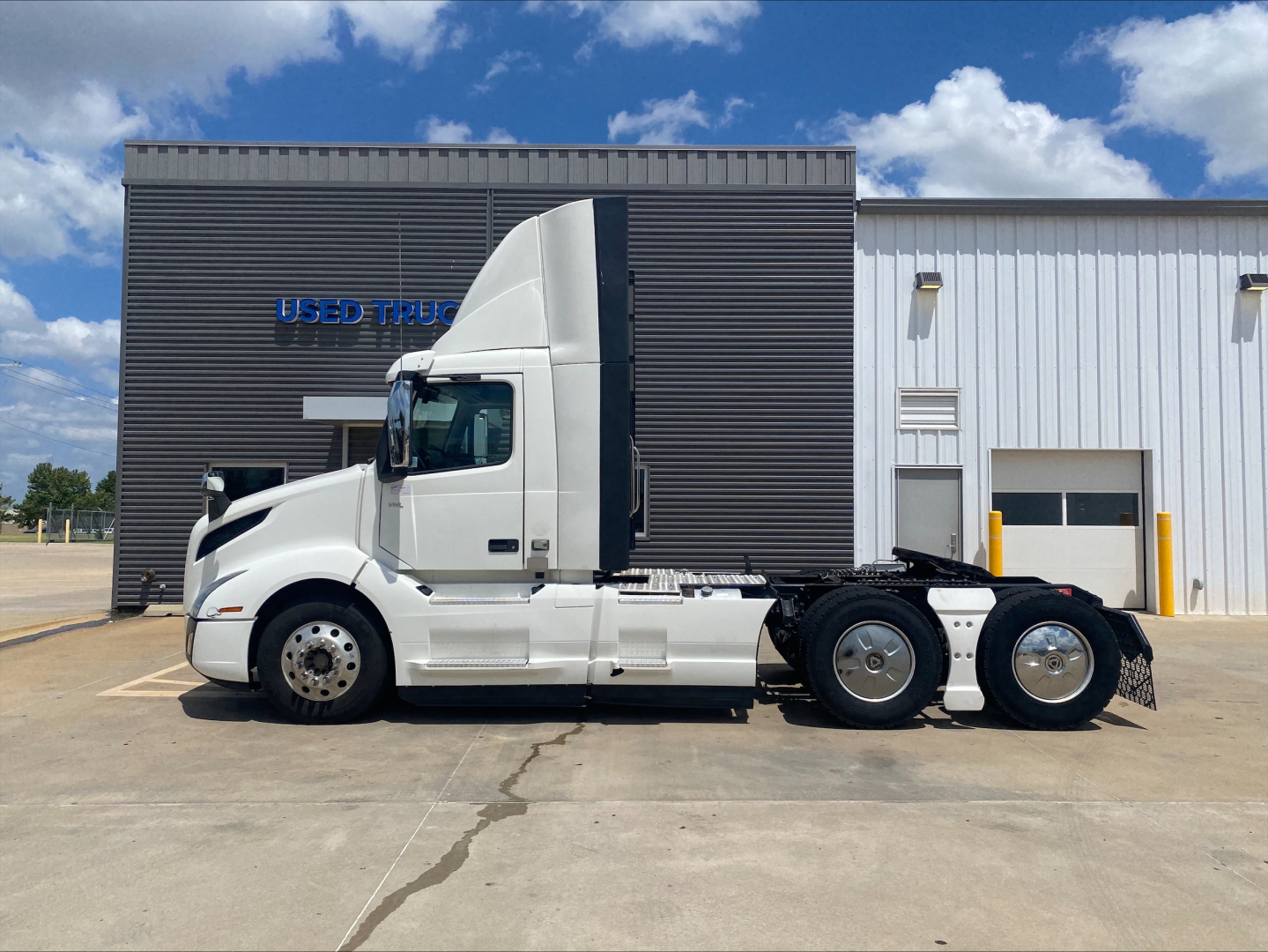 Volvo VNL300 daycab tractor in white, side view, 3-axle chassis, parked in front of a building with blue sky
