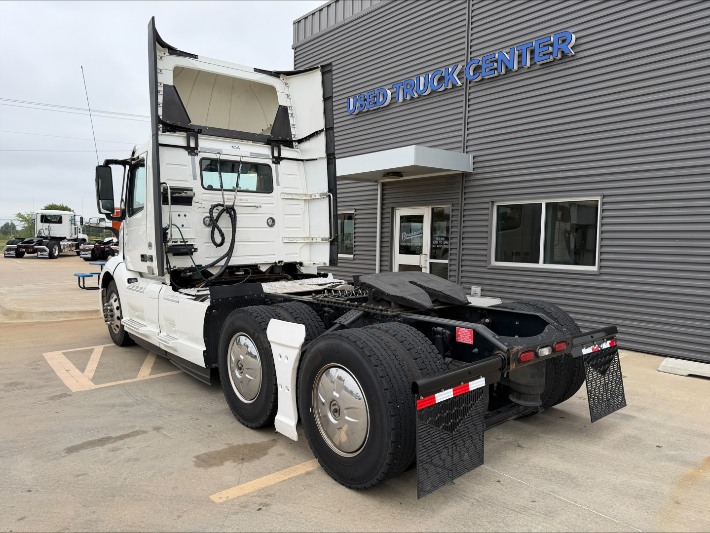 2019 Volvo VNL300 truck from rear-left side showing tractor cab with tagline 'USED TRUCK CENTER' on building. Visible text on truck includes none legible; environment shows rear wheels and fifth wheel.