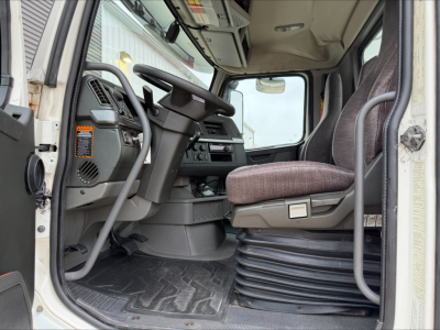 Truck cab interior showing steering wheel, driver seat, and dashboard of a Volvo VNL300. Floor mat, gear shifter area, and entry steps visible.