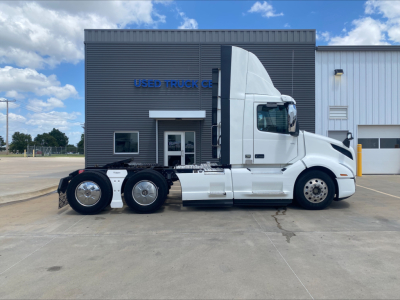 Volvo VNL300 daycab side view showing tractor with sleeper cab, six wheels, white paint, no visible damage, parked in front of a building