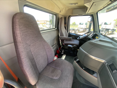 Interior of a 2019 Volvo VNL300 cab showing front seats, dashboard, and steering wheel from the passenger side angle; visible window and exterior trucks outside