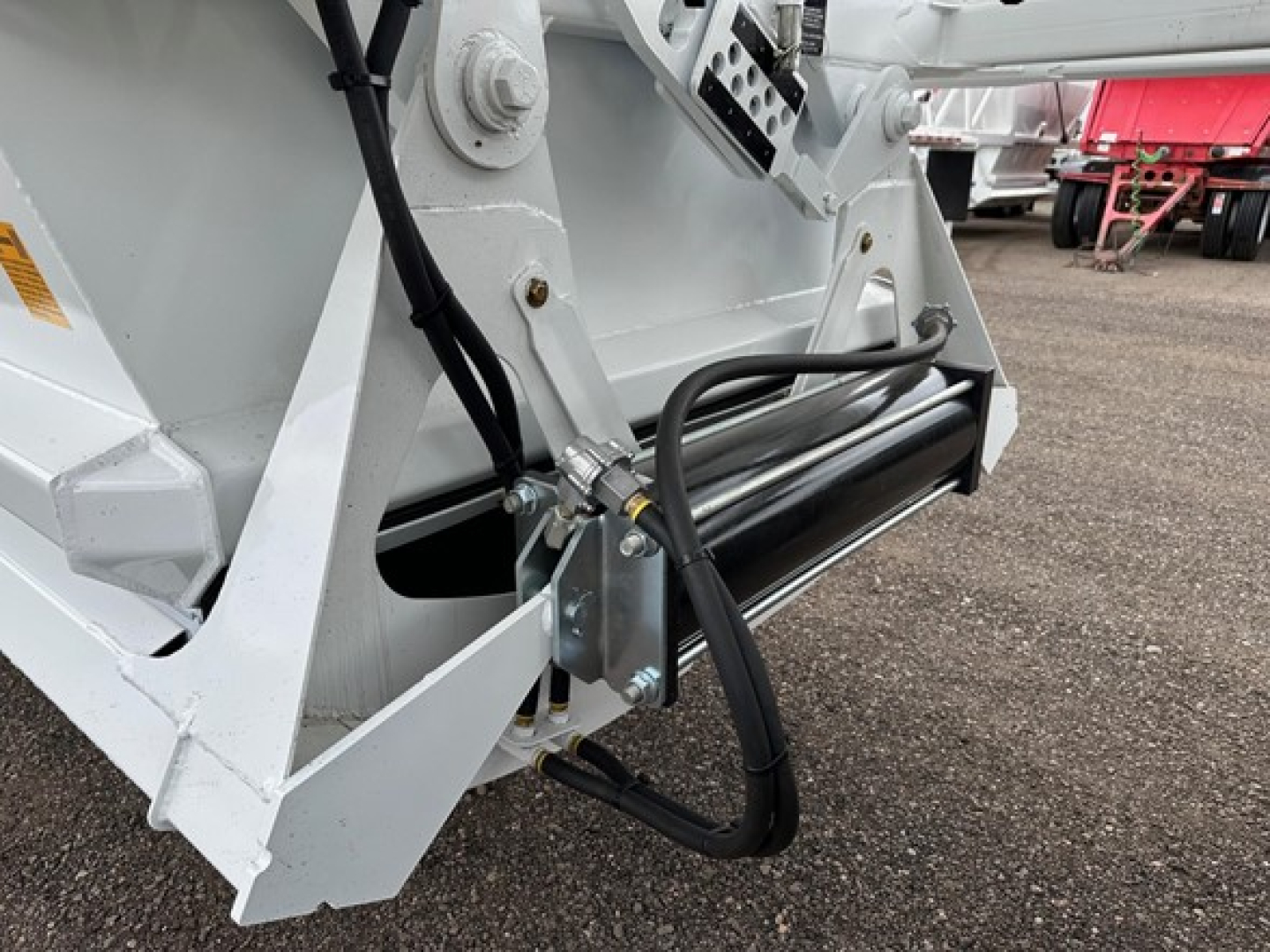 Front lower view of a dump trailer hitch area showing hydraulic hose, metal roller, and welded steel frame with light gray paint.