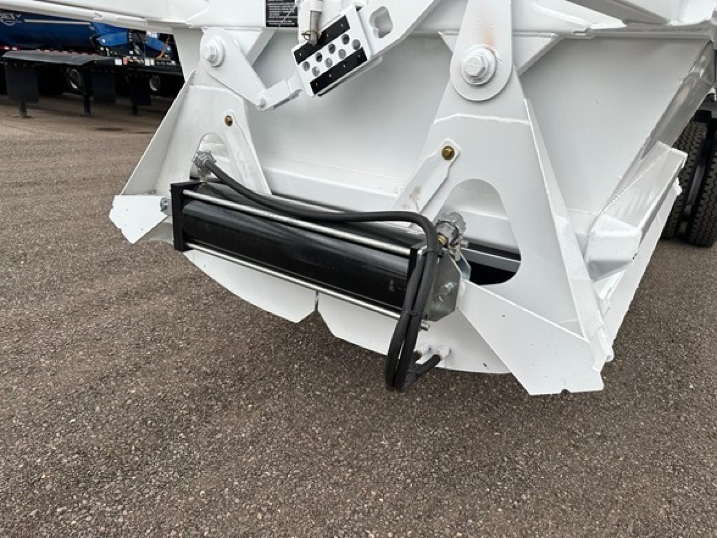 Dump trailer component showing hydraulic cylinder and white framing with black hydraulic hose assembly.