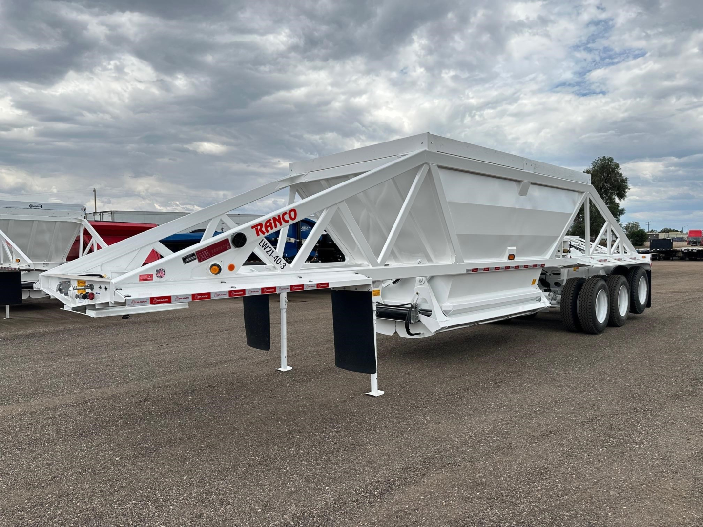 Ranco LW21-40-3 lowboy trailer showing triple axle configuration and white frame with site soil road in background.