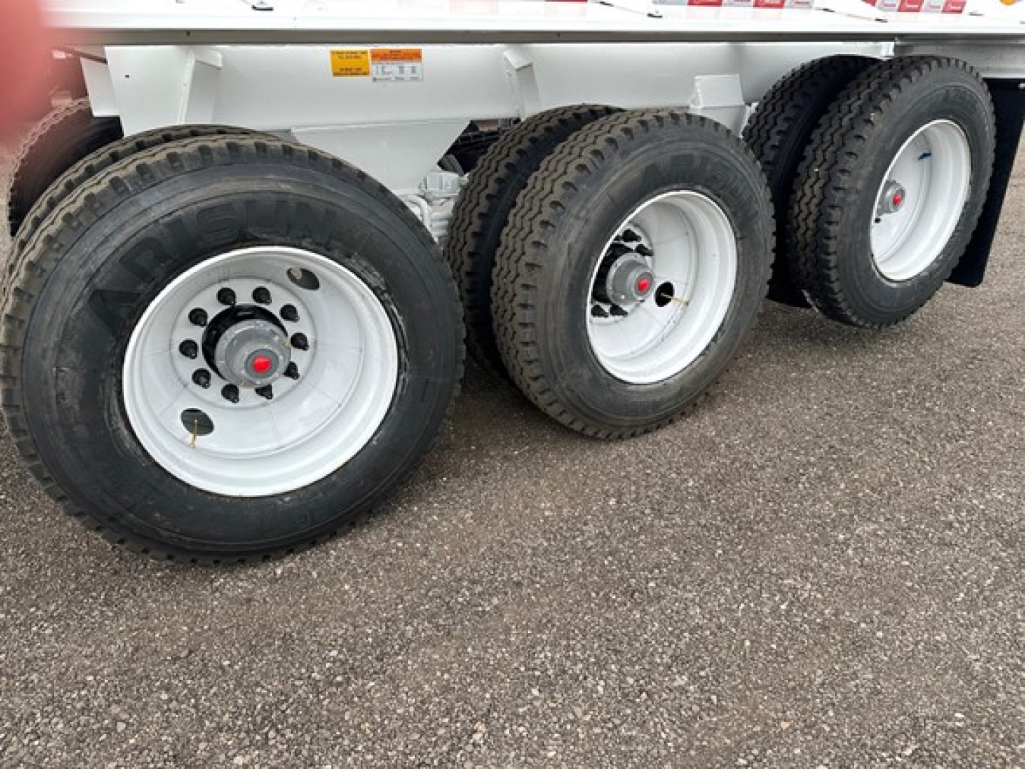 Three trailer wheels with white rims and black tires, showing the side of a dump trailer.