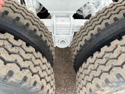 Dual rear wheels of a dump trailer chassis with heavy tread tires and a white metal suspension hub visible between the tires.