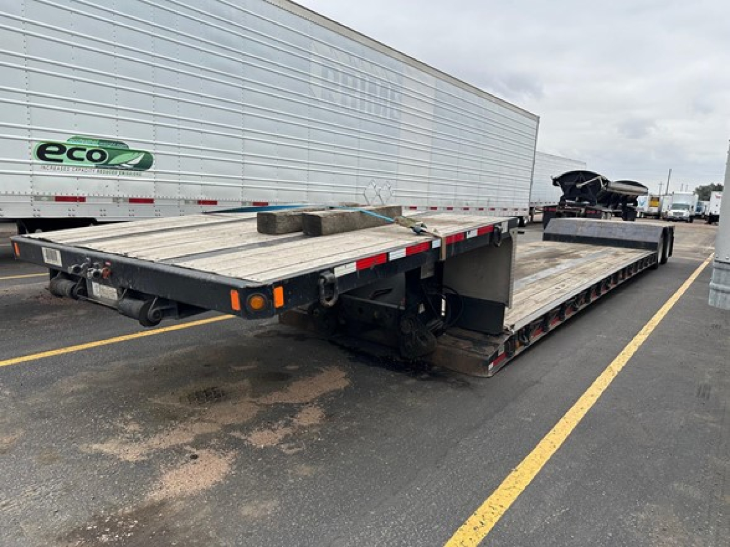 Flatbed punch trailer showing two deck sections with steel surface and wooden blocks; no visible writings on deck, background includes a white trailer with eco logo.