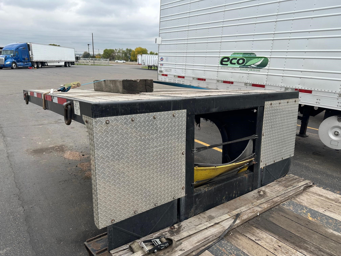 Flatbed trailer with diamond plate toolboxes on both sides and open center; large trailer with black frame and metal diamond-plate storage boxes.