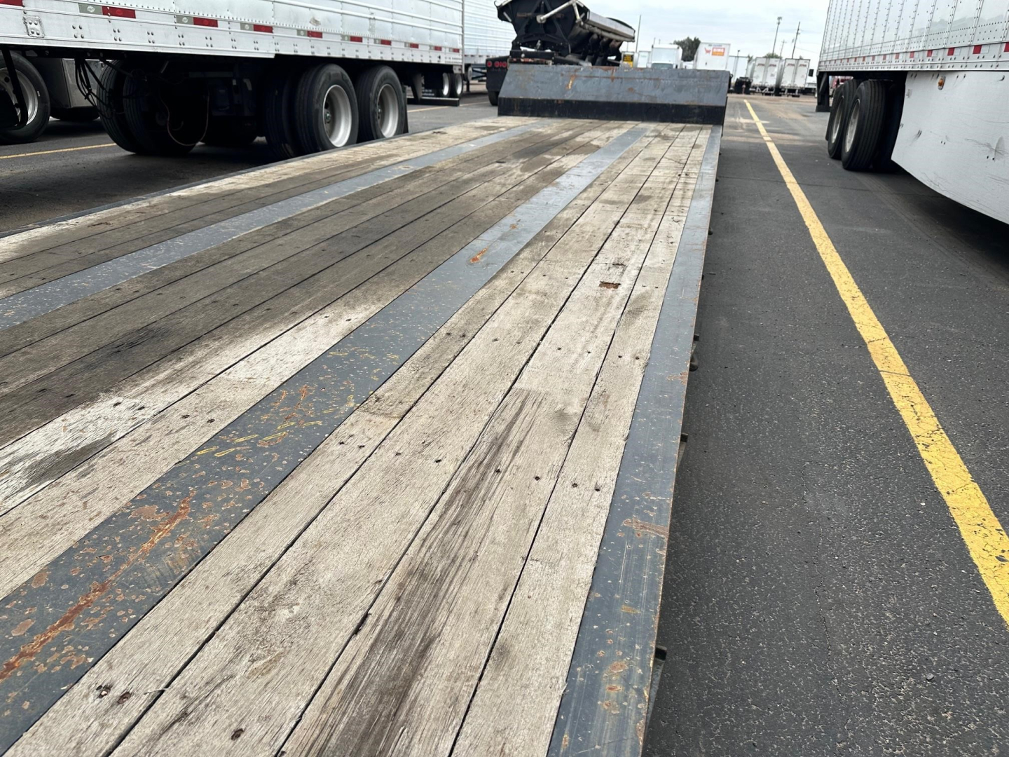 Fontaine Renegade trailer with long wooden deck and side rails, viewed from front showing extendable gooseneck area and surrounding trailers.