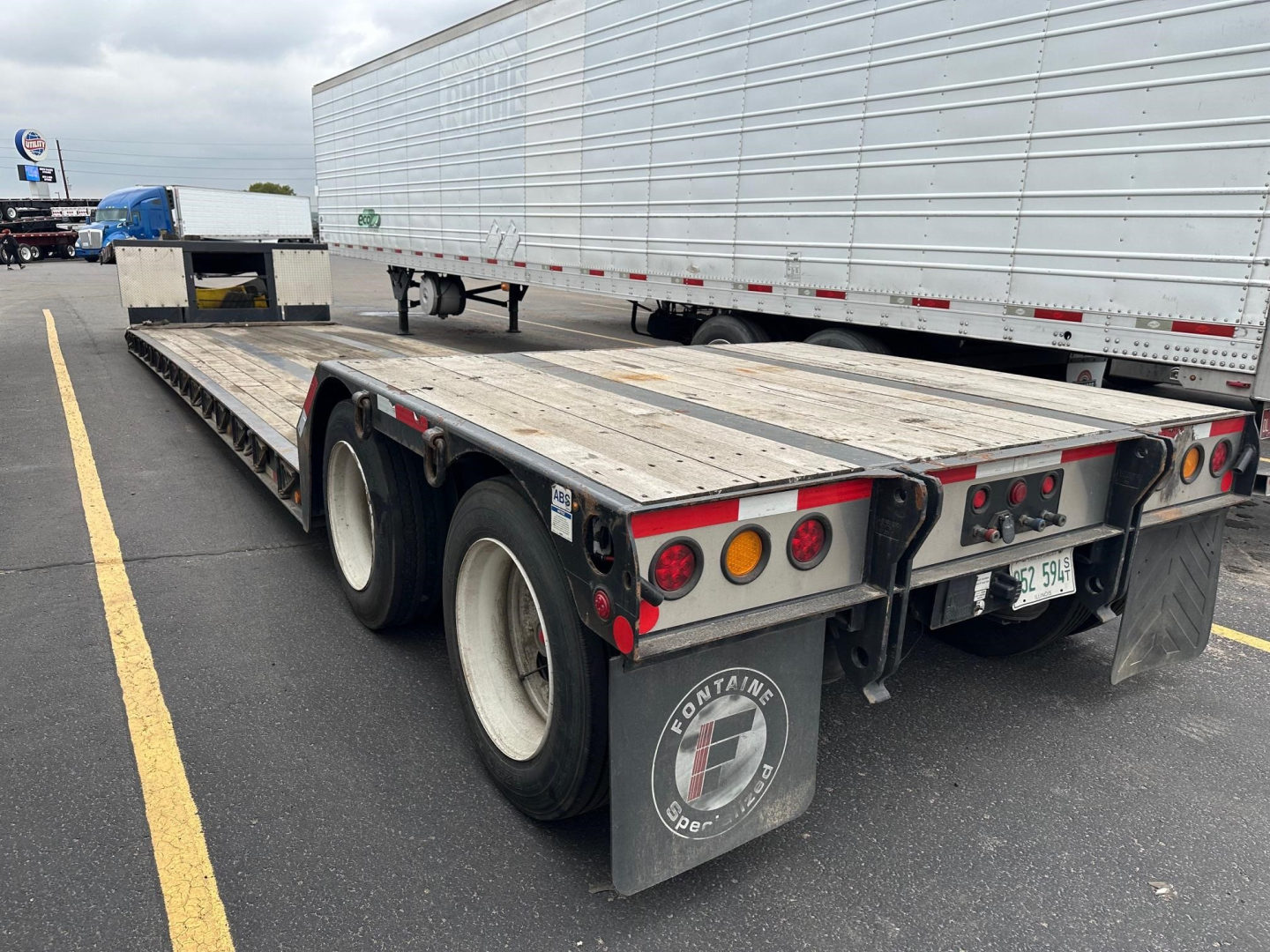 Fontaine Renegade trailer with dual rear axles in a parking lot, flatbed surface, undercarriage visible, rear lights and mudflaps with Fontaine logo.