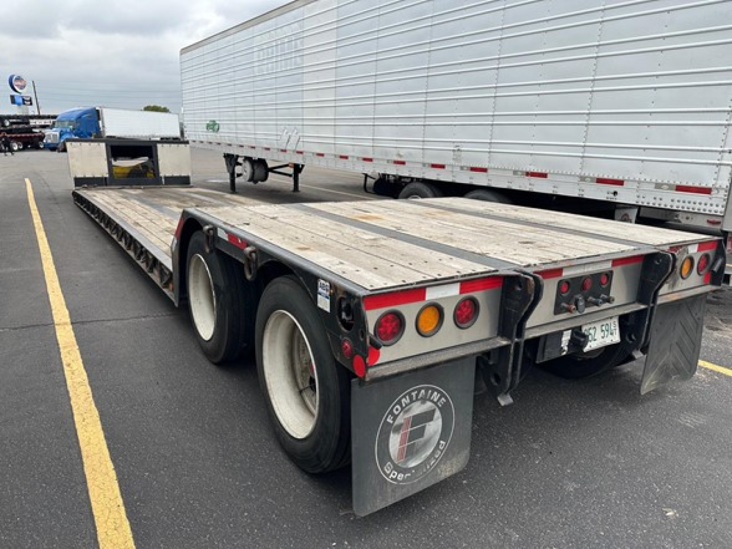 Fontaine Renegade trailer with triple-axle rear, flatbed with metal deck, rear taillights, mudflaps, and Fontaine logo on the mudflap.